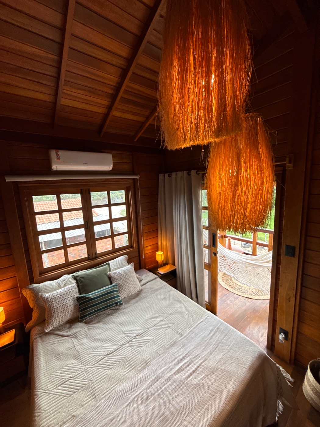 Suíte de casal — cama, ar-condicionado e rede ao fundo